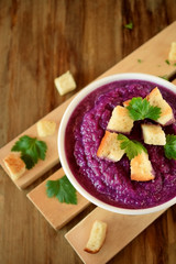 Cream soup made of red cabbage with croutons and parsley on wooden table