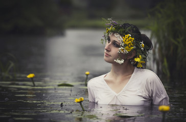 Art Woman with wreath on her head in a swamp in the woods. Wet witch Girl in the lake, mystical...