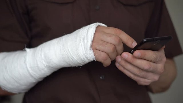 A man with a broken right hand in a plaster uses a smartphone to search for information. A fracture of the hand led to disability. Health insurance. Hands close-up