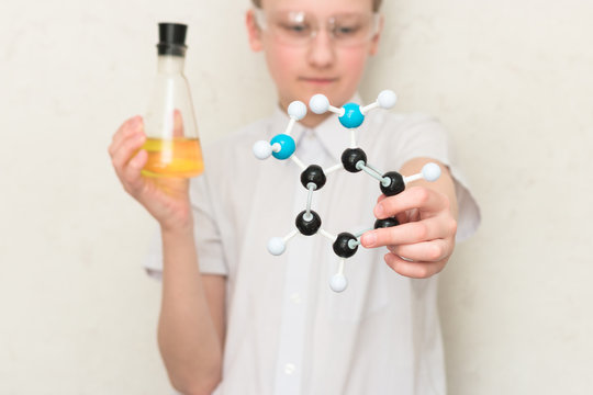 A teenager boy in a chemistry class holds a flask with chemicals and a plastic model of a molecule. Science. STEM education. School lab.