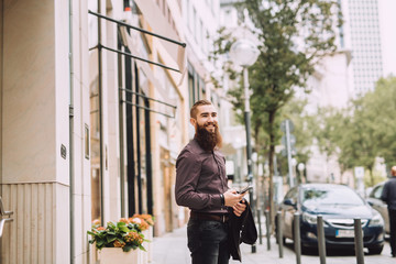 Fototapeta na wymiar Young man with the beard uses a mobile phone in the city beside the office