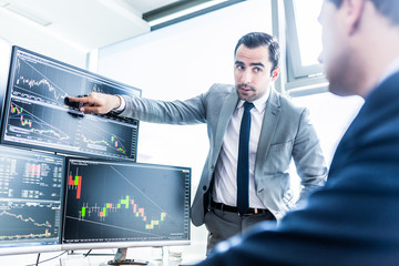 Businessmen trading stocks online. Stock brokers looking at graphs, indexes and numbers on multiple...