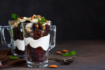 Chocolate dessert in a glass with vanilla cream and nuts on a dark background.