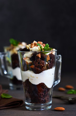 Chocolate dessert in a glass with vanilla cream and nuts on a dark background.