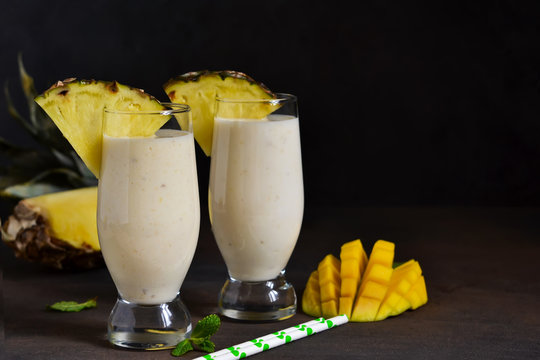 Milk cocktail with vanilla ice cream, pineapple and mango on a dark background.