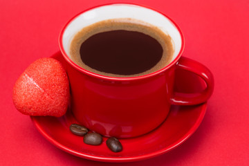 red cup with black coffee with foam on a red background, marshmallow in the shape of a heart lays on a saucer, the concept of love