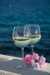 Two glasses with cold white wine served outside on terrace with pink tropical flowers, luxury resort with sea view, romantic vacation
