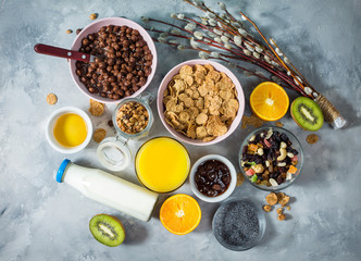 Healthy breakfast with bowl of cereal, orange juice, granola, milk, jam and fruits on concrete background. Balanced diet. Top