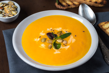 Fried pumpkin and carrot soup with cream and pumpkin seeds on a dark wooden background. Greens and pumpkins seeds.