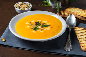 Fried pumpkin and carrot soup with cream and pumpkin seeds on a dark wooden background. Greens and pumpkins seeds.