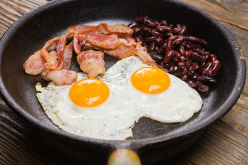 Bacon,Egg and bean. Salted egg and sprinkled with black pepper. English breakfast. Grilled bacon, two eggs and beans in pan on wooden table
