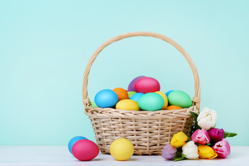 Colorful easter eggs in basket with tulips on wooden table