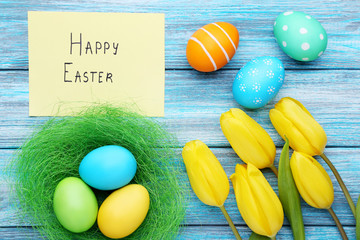 Inscription Happy Easter with painted eggs and yellow tulips on wooden table