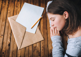 A cute little girl is writing a letter. The girl put her head on the table next to the letter and...