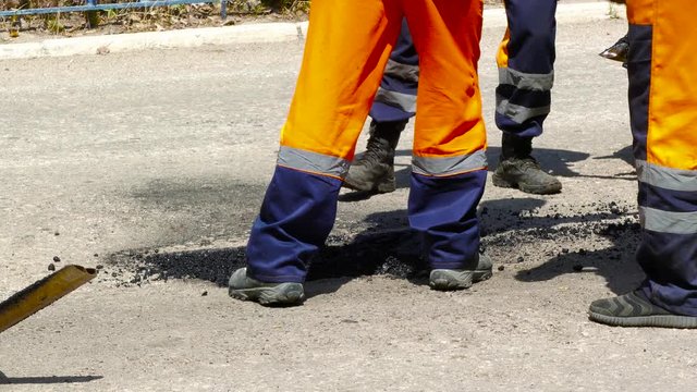 A group of workers using shovels lay asphalt in a hole in the road surface