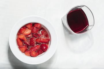 Strawberry in a white bowl, with glass of red wine, shooted from above
