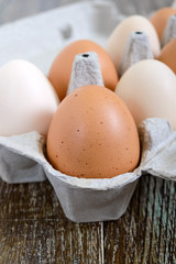 Fresh raw chicken eggs in carton egg box on wooden background. Close-up view on brown and white eggs. The main ingredient for many dishes.