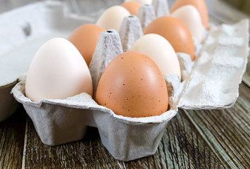 Fresh raw chicken eggs in carton egg box on wooden background. Close-up view on brown and white eggs. The main ingredient for many dishes.