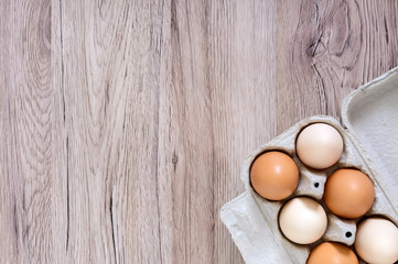 Fresh raw chicken eggs in carton egg box on wooden background. The top view on brown and white eggs. Close-up view. The main ingredient for many dishes. Free space for inscriptions, notes.