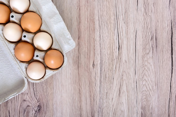 Fresh raw chicken eggs in carton egg box on wooden background. The top view on brown and white eggs. Close-up view. The main ingredient for many dishes. Free space for inscriptions, notes.