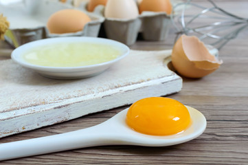 Fresh farm eggs on a wooden rustic background. Separated egg white and yolks, broken egg shells. Whipping eggs with whisk. Preparation of food from chicken eggs.