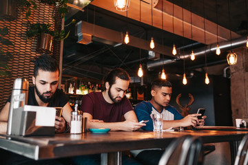 Social media addiction concept. Mixed race friends looking at their phones in lounge bar