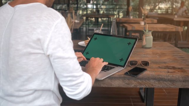 closeup of male hands working on a laptop with green screen in cafe