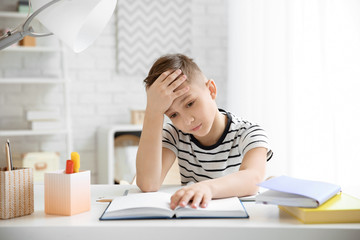 Little boy suffering from headache while doing homework at table indoors