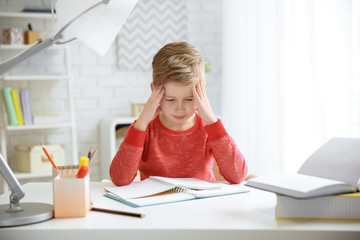 Little boy suffering from headache while doing homework at table indoors