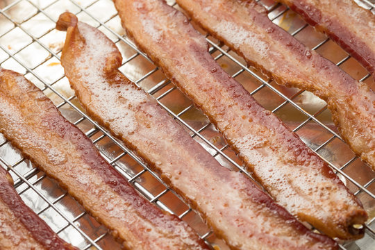 Rows of fried bacon strips with grease foam, on a wire cooling rack