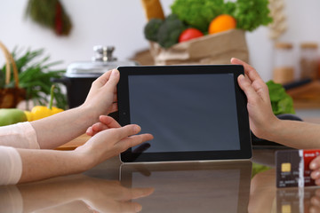 Closeup of human hands cooking in kitchen. Women discuss a menu using tablet computer. Copy space area at touch pad. Healthy meal, vegetarian food and lifestyle concepts