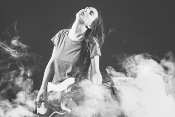 Beautiful rock girl playing bass guitar in smoke