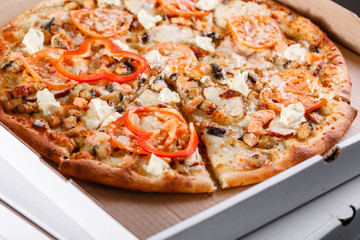 Pizza box delivery concept. Open box with hot tasty italian sliced pizza with salmon, eel, seafood, olives, basil, tomato, mushrooms.