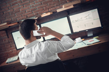 Young male trader at office work concept sitting talking on smartphone back view