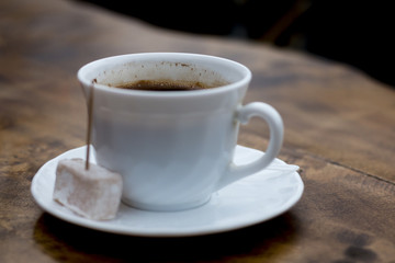 Cup of Turkish coffee served with locum with tootpick in it, wood table, dark background and great contrast