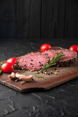 Smoked salami on a black table and a brown board. Sausages with rosemary, garlic and pepper and tomato cherry, dill, parsley.