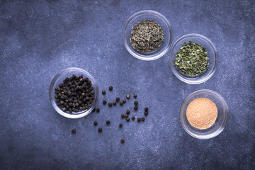 Obraz na płótnie Canvas Flat lay of spilled black peppercorns, beside glass dishes of Italian spices on slate