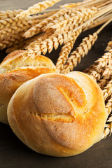 Bunch of whole, fresh baked wheat buns with wheat ears on dark wooden table