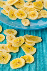 Heap of dried banana chips snack on blue turquoise plate and mat