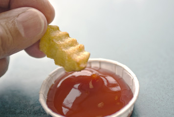 hand dipping fench fry into ketchup