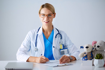 Beautiful young smiling female doctor sitting at the desk.