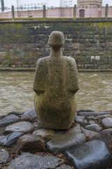 a figure of stone sitting on the river bank