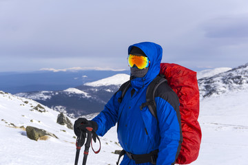 Fototapeta na wymiar mountaineer in mirror wind-proof glasses and a windproof mask with a backpack on a background of a winter mountain landscape