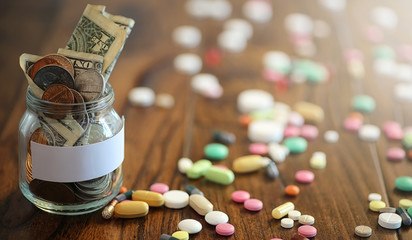 Drugs and coins in a glass jar on a wooden floor. Pocket savings