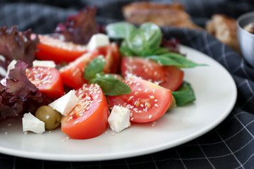 Salad with tomatoes and basil served on white plate, closeup
