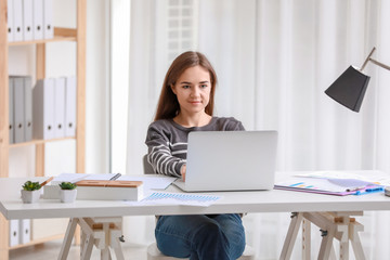 Young woman working with laptop at table in office