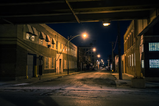 Dark and eerie Chicago urban city street night scenery with elevated CTA train tracks, vintage industrial warehouses and factories.
