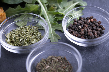 Glass ingredient dishes of dried parsley seasoning beside black peppercorns