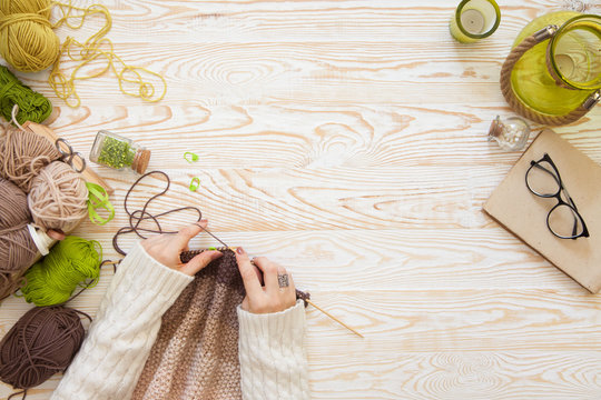 A woman knits a white and broun knitted fabric of woolen yarn. Knitting needles. Aged background. Green and white.