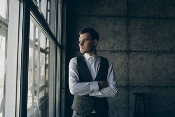 Young beautiful man staying  near the window on a gray background.